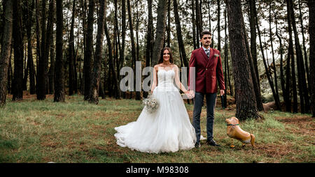 Happy bride and groom standing in forest with funny dog-shaped balloon Stock Photo