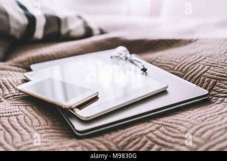 Stack of three mobile devices on bed Stock Photo