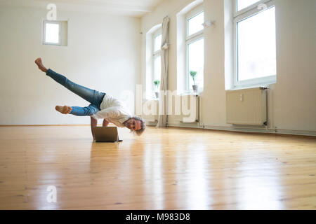 Mature man doing a handstand on floor in empty room looking at tablet Stock Photo