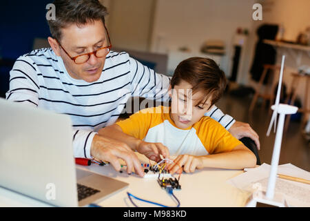 Father and son assembling a construction kit with laptop and wind turbine model Stock Photo