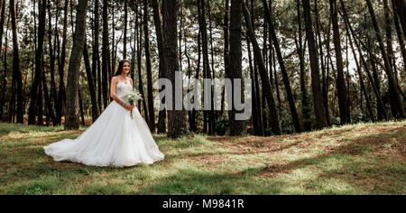 Smiling bride holding bouquet of flowers in forest Stock Photo