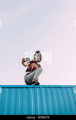 Young woman with basketball taking a selfie on container Stock Photo