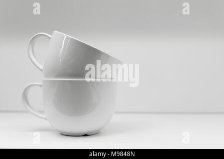 Two mugs on a white background are standing. A black and white mug is next on the table. Stock Photo
