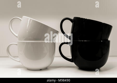 Two mugs on a white background are standing. A black and white mug is next on the table. Stock Photo