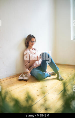 Mature woman sitting on floor using tablet Stock Photo