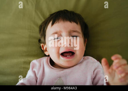 Portrait of crying baby girl lying on bed Stock Photo