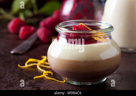 Glass of pudding with vanilla sauce and raspberry sauce garnished with raspberries and orange zest Stock Photo