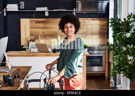 Portrait of smiling young woman with bicycle in modern office Stock Photo