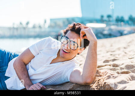 Portrait of happy young man lying in sand on the beach Stock Photo
