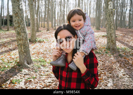 Mother carrying her daughter on her shoulders in park Stock Photo
