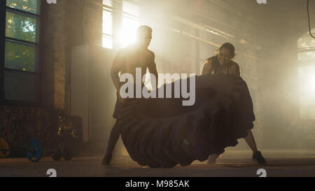 Fit Athletic Woman Lifts Tire Under Supervision of Her Partner/ Trainer, as Part of Her Cross Fitness/ Bodybuilding Gym Training. Stock Photo