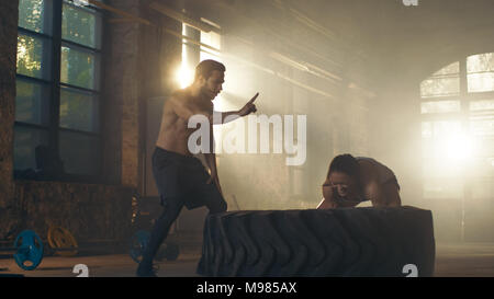 Fit Athletic Woman Lifts Tire Under Supervision of Her Partner/ Trainer, as Part of Her Cross Fitness/ Bodybuilding Gym Training. Stock Photo