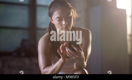 Beautiful Athletic Brunette Uses Smartphone while Resting on the Bench after Her Intensive Cross Fitness Bodybuilding Gym Training. Stock Photo