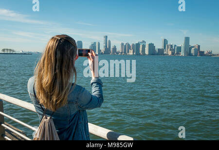 USA, New York, woman taking cell phone picture of New Jersey skyline
