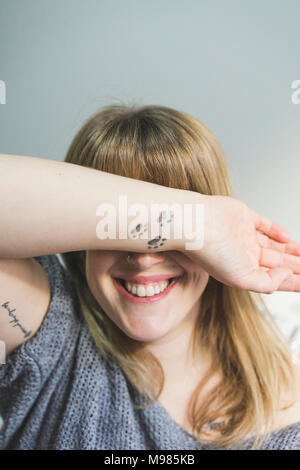 Laughing tattooed woman covering eyes with her arm Stock Photo