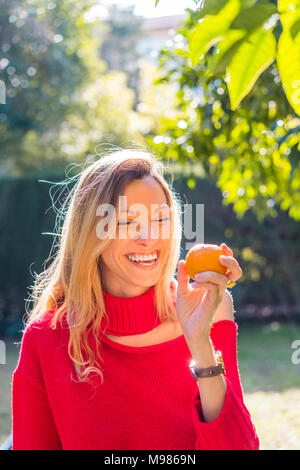 Laughing young woman holding mandarin in a garden Stock Photo
