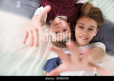 Top view of two smiling brothers lying on bed reaching out their hands Stock Photo