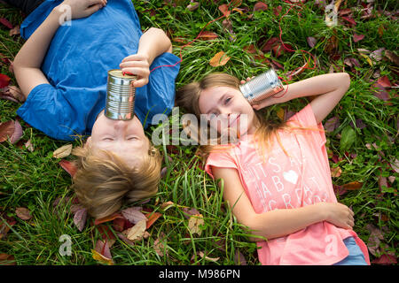 Boy and girl on a meadow having fun with tin can phone Stock Photo