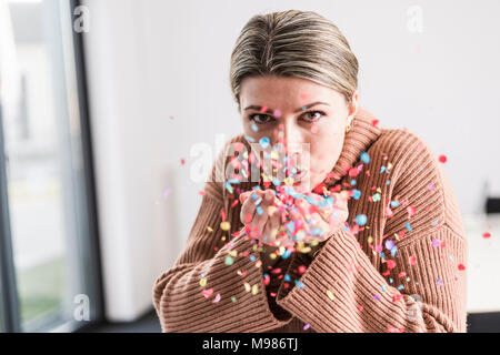 Portrait of young woman blowing confetti in the air Stock Photo