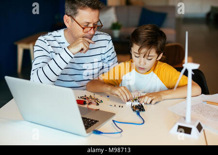 Father and son assembling a construction kit with laptop and wind turbine model Stock Photo