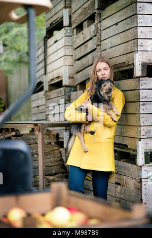 Woman on a farm standing at wooden boxes holding dog Stock Photo