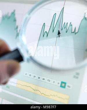 Investor analysing line graph on computer screen with magnifying glass Stock Photo