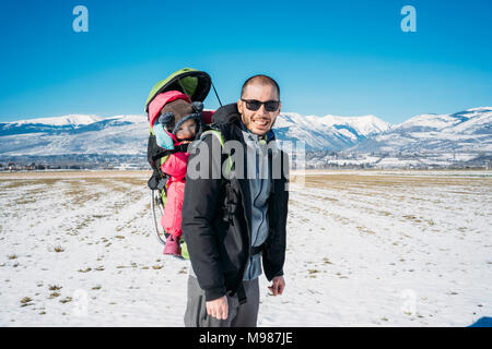 Spain, Puigcerda, father with baby girl in a kid carrier backpack during a hike at winter Stock Photo