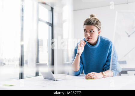 Young woman with laptop at desk in office thinking Stock Photo
