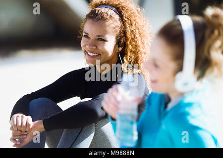 Two smiling sportive young women having a break listening to music Stock Photo