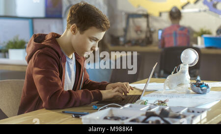 Smart Young Boy Works on a Laptop For His New Project in His Computer Science Class. Other Children Learning in the Background. Stock Photo