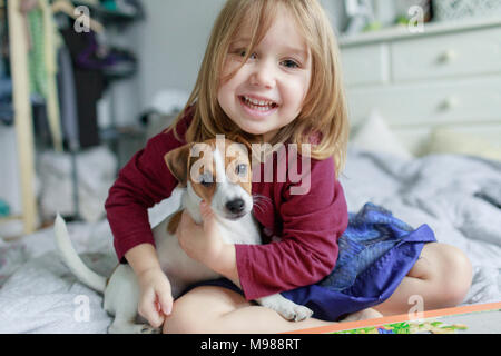 Portrait of happy little girl crouching on bed with Jack Russel Terrier puppy Stock Photo