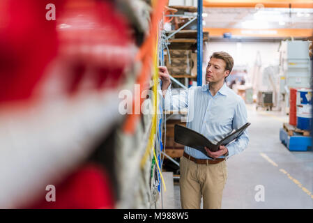 Man in factory storeroom holding folder checking shelf Stock Photo