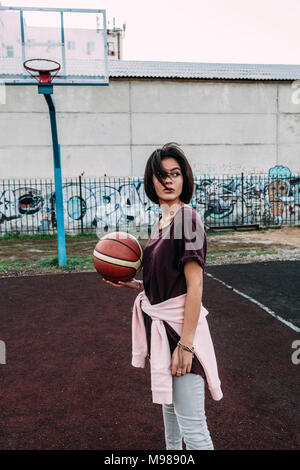 Young woman standing with basketball on outdoor court Stock Photo