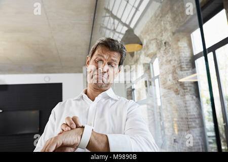 Sceptical businessman in office using smartwatch Stock Photo
