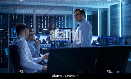 Team of Technical Moderators Have Discussion in Monitoring Room. System Control Room is full of Working Displays and Has Servers Racks. Stock Photo