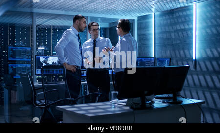 Team of Technical Moderators Have Active Discussion in Monitoring Room. System Control Room is full of Working Displays Showing Various Data Stock Photo