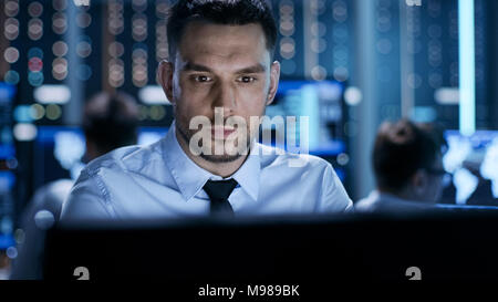 Close-up of a Professional Technical Controller Sitting at His Desk with Multiple Displays Before Him. In the Background His Colleagues Working Stock Photo