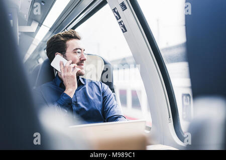 Smiling businessman in train on cell phone Stock Photo
