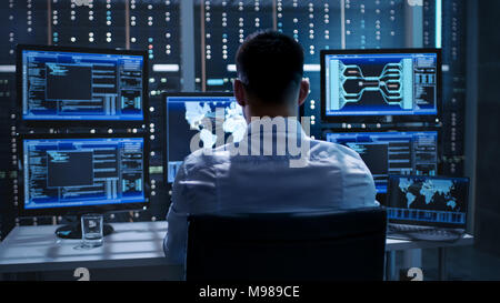 System Security Specialist Working at System Control Center. Room is Full of Screens Displaying Various Information. Stock Photo