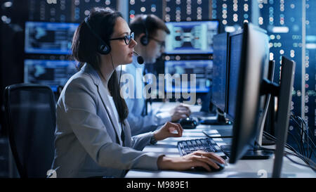Female working in a Technical Support Team Gives Instructions with the Help of the Headsets. In the Background People Working and Monitors Show Info Stock Photo