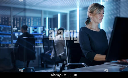 Female IT Engineer Works on Her Desktop Computer in Government Surveillance Agency. In the Background People at Their Workstations with Screens Stock Photo