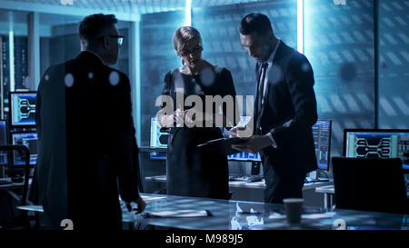 Team of Chief Engineers Have Emergency Meeting in System Controls Center. Man Holds Tablet. Computers in the Room Have Various Information Stock Photo