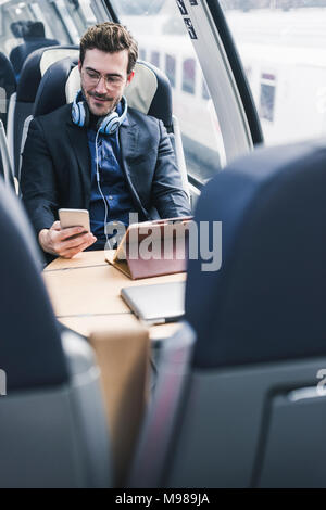Businessman in train with cell phone, headphones and tablet Stock Photo