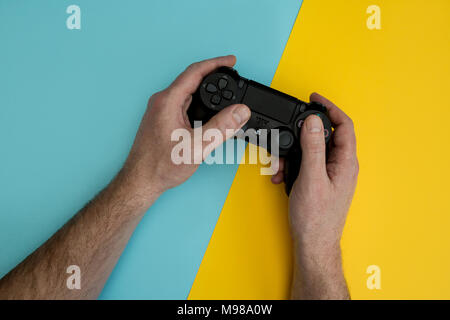 LONDON - MARCH 22, 2018: Man playing video games holding PlayStation gaming controller in hands Stock Photo