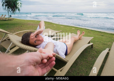 Caucasian woman in chair near beach holding her husband hand. Follow me concept. Having great vacation near seashore in hotel Stock Photo