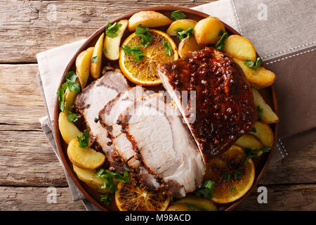 Spicy pork baked with potatoes, oranges and apples close-up on a plate. Horizontal top view from above Stock Photo