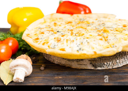 Tasty pizza four cheeses on wooden stand in the form of hemp near tomatoes, mushroom and pepper on wooden desk Stock Photo