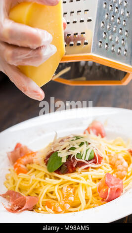 https://l450v.alamy.com/450v/m98am5/close-up-of-hands-in-gloves-rub-cheese-on-a-grater-above-tasty-spaghetti-pasta-with-shrimps-tomato-sauce-and-basil-in-white-plate-surrounded-by-veget-m98am5.jpg