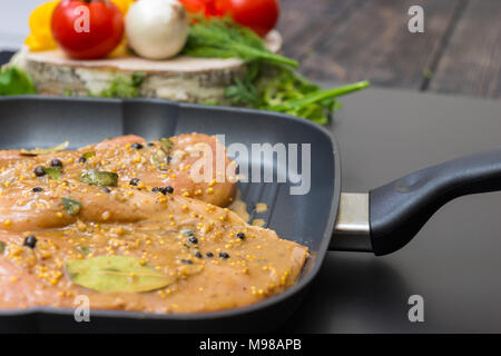 Close up of marinated chicken meat on a grill pan near pepper, onions, tomatoes, dill and parsley on a wooden board on a gray background Stock Photo