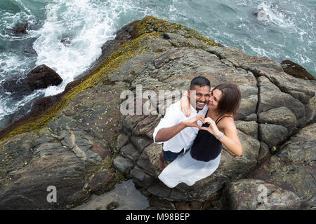 Caucasian girl and her handsome boyfriend making shape of heart sign by their hands on background of ocean. Happy joyful family. Love concept. Laughin Stock Photo